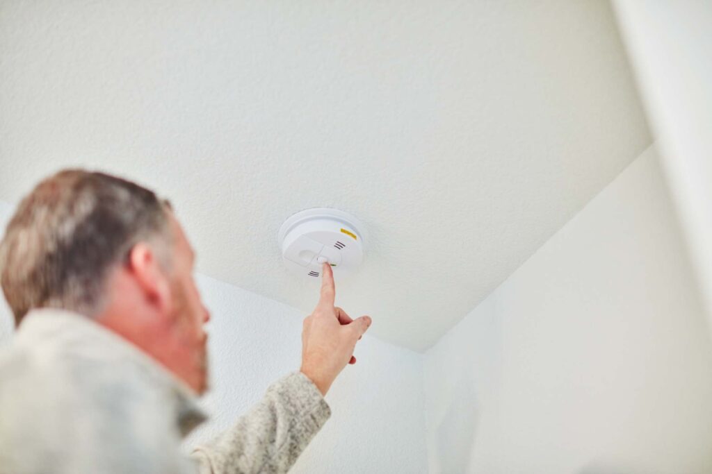 Middle-aged white man checks the carbon monoxide and smoke detector on the ceiling of his home.