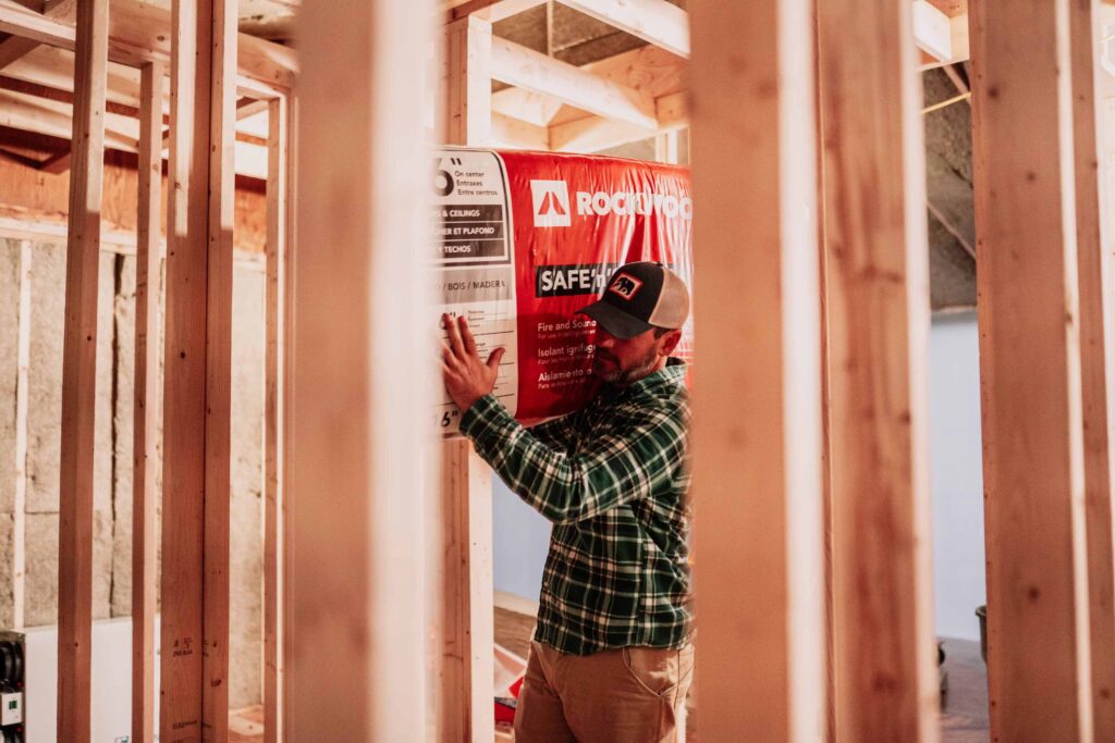 Man in plaid adds a bag of Rockwool insulation to a new home build.